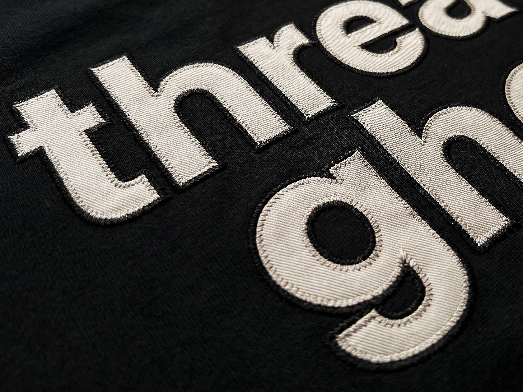 Macro of embroidered threadghost lettering in cream thread on black fleece