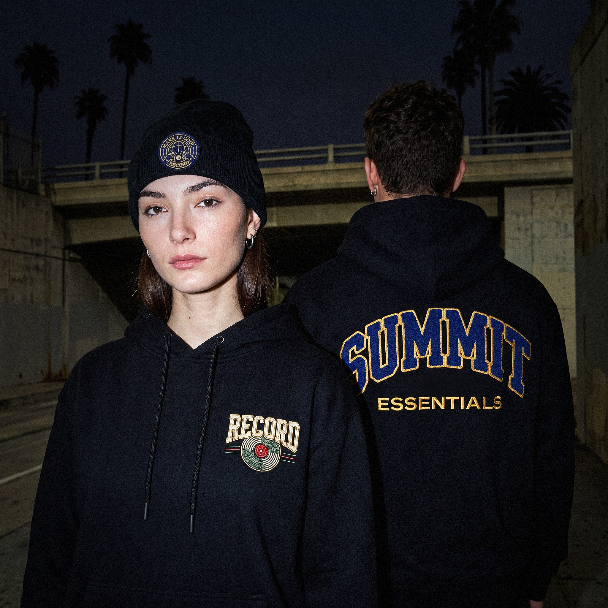 A black hoodie with a left-chest embroidered crest and a full-back arched wordmark