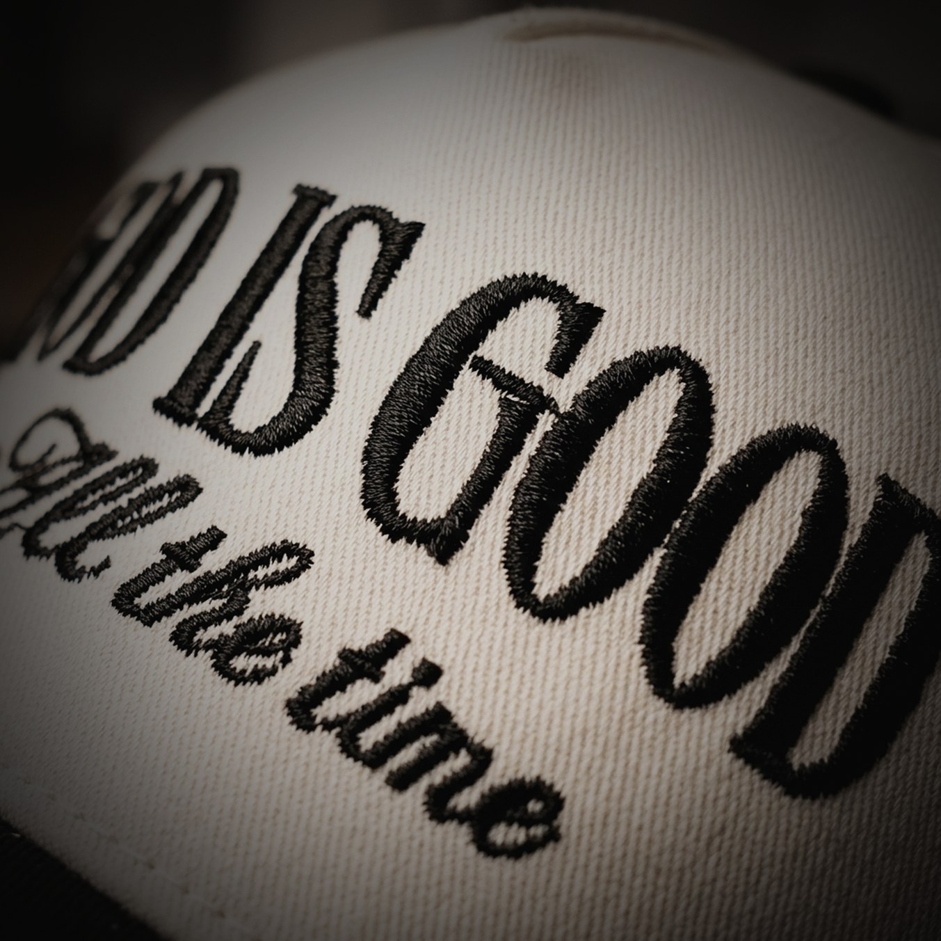 Black embroidered script lettering on a cream cap