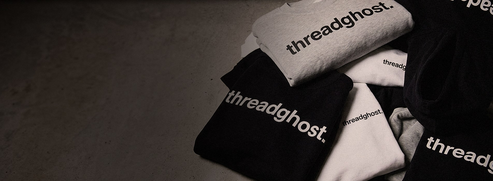 Black, white and grey threadghost tees and crewnecks piled on concrete