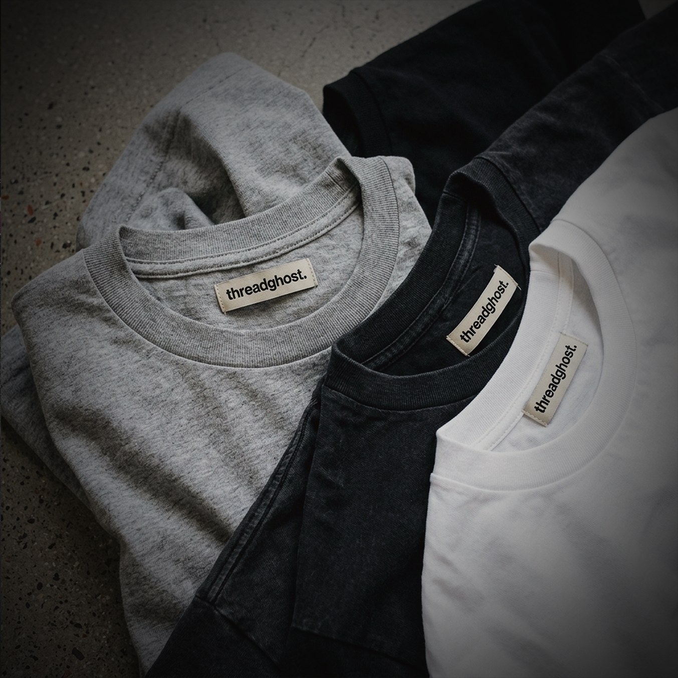 Grey, black and white threadghost tees folded on concrete